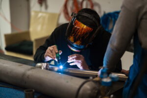 man performing microplasma welding on a metal pipeline